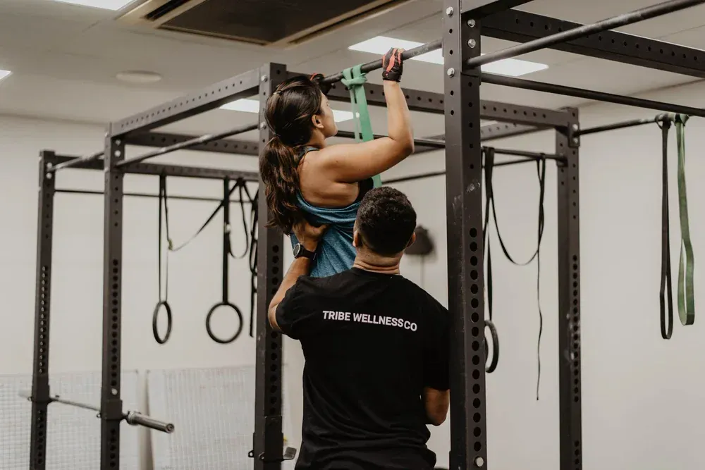 A member doing pull-ups with a coach spotting at Tribe Wellness Co